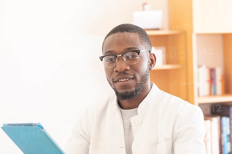 Young black doctor with smock and tablet explaining in the surgery