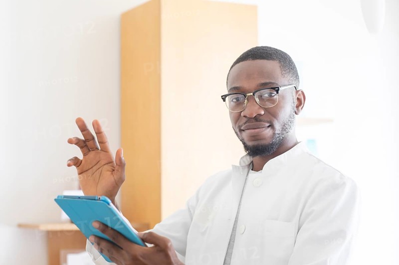 Young black doctor with smock and tablet explaining in the surgery