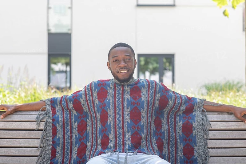Young black man sitting on bench with African poncho
