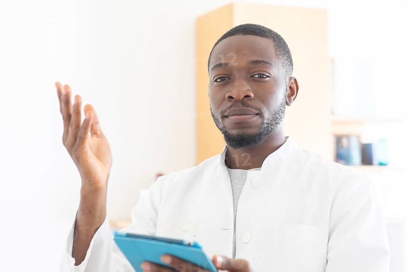 Young black doctor with smock and tablet explaining in the surgery