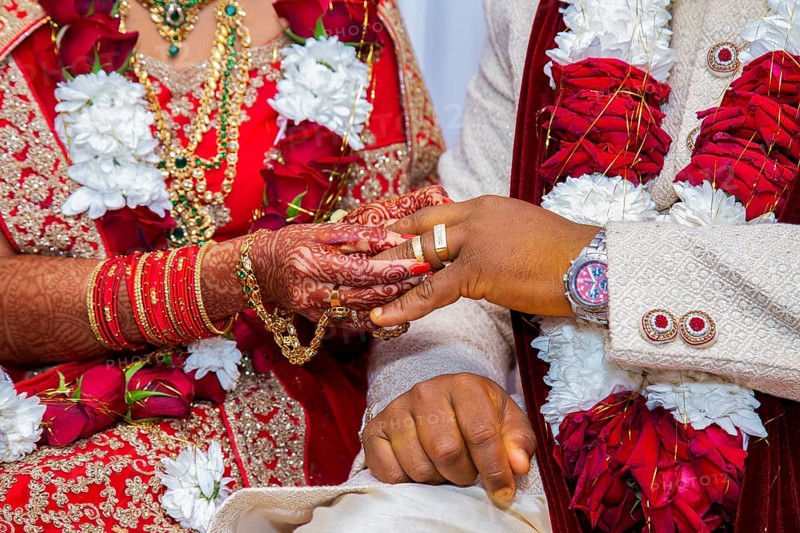 Bride with bridal jewelry and henna decoration on her hand attaches ring to the groom's finger at traditional religious ceremony at a Hindu wedding