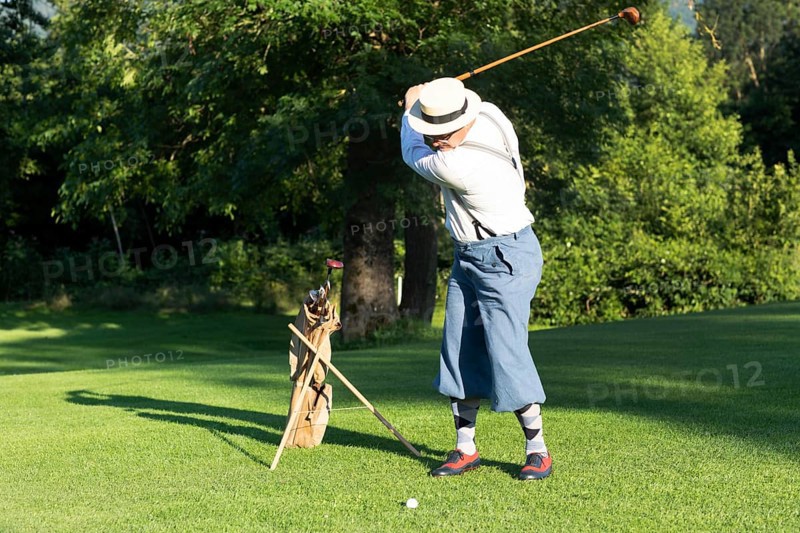 Older man in straw hat and knickerbockers playing hickory golf on a golf course