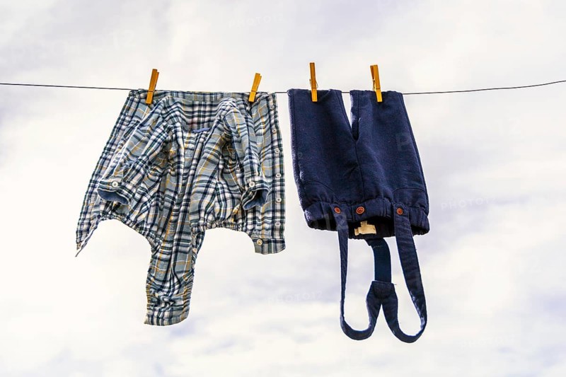 Elegant baby trousers and shirt pinned with wooden pegs against cloudy sky