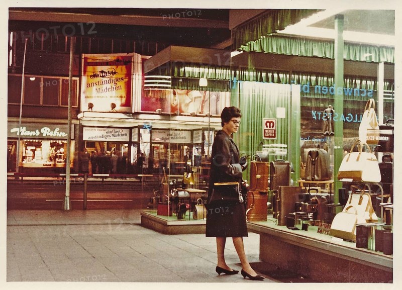 Stuttgart at night in 1963: A young woman with a coat and handbag looks at the display of handbags and suitcases in a leather goods shop