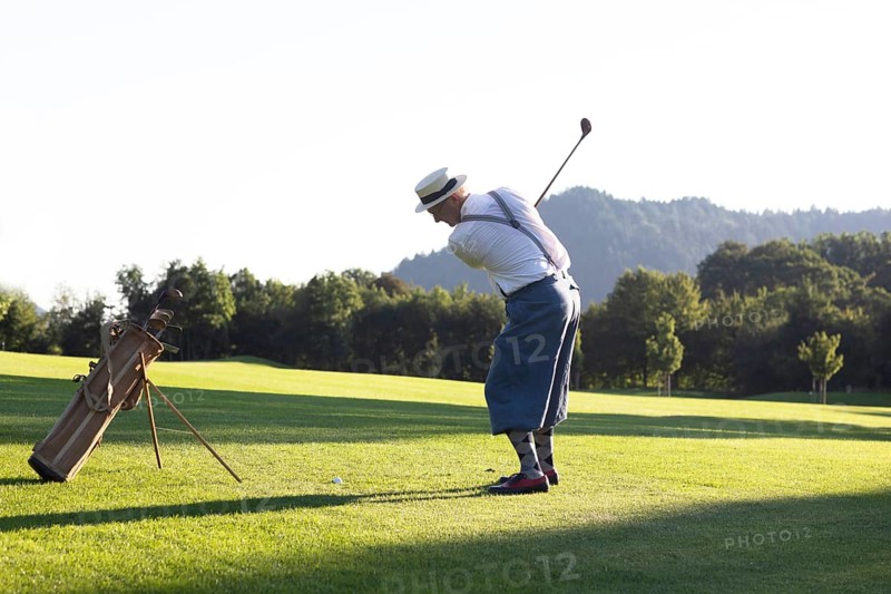 Older man in straw hat and knickerbockers playing hickory golf on a golf course