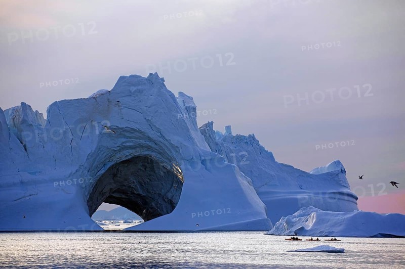 Kayaks in front of huge iceberg with cave