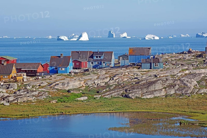 Wooden houses and rocks in front of a bay filled with icebergs