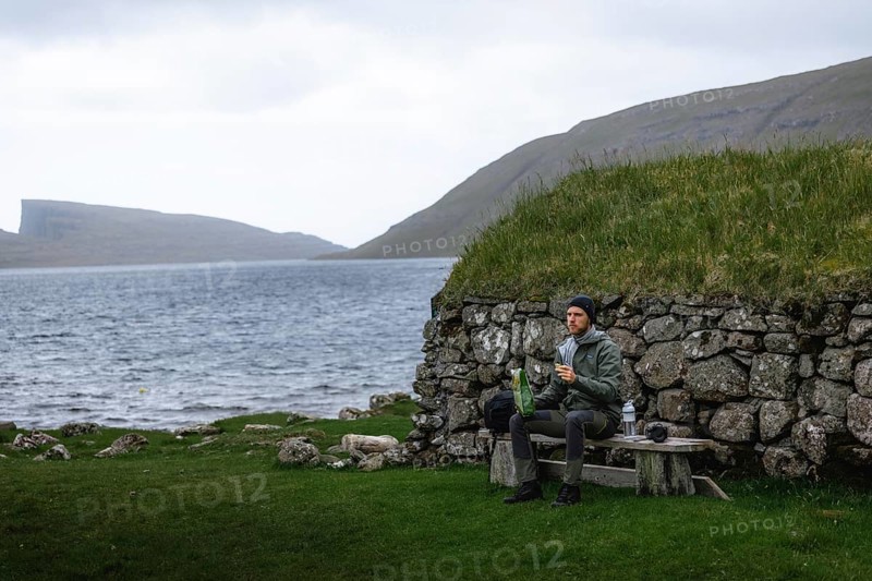 Hiker eating biscuits on a bench in front of a stone hut