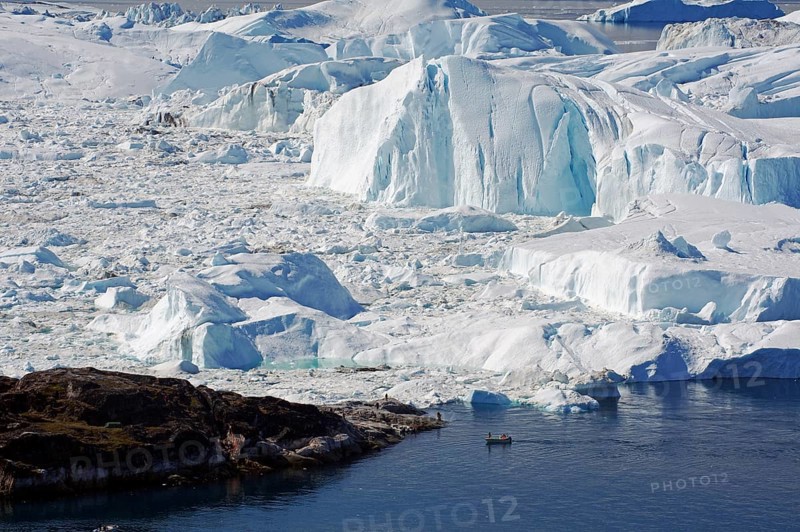 Small fishing boat in front of huge icebergs