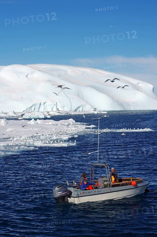 Small fishing boat in front of huge icebergs and drift ice