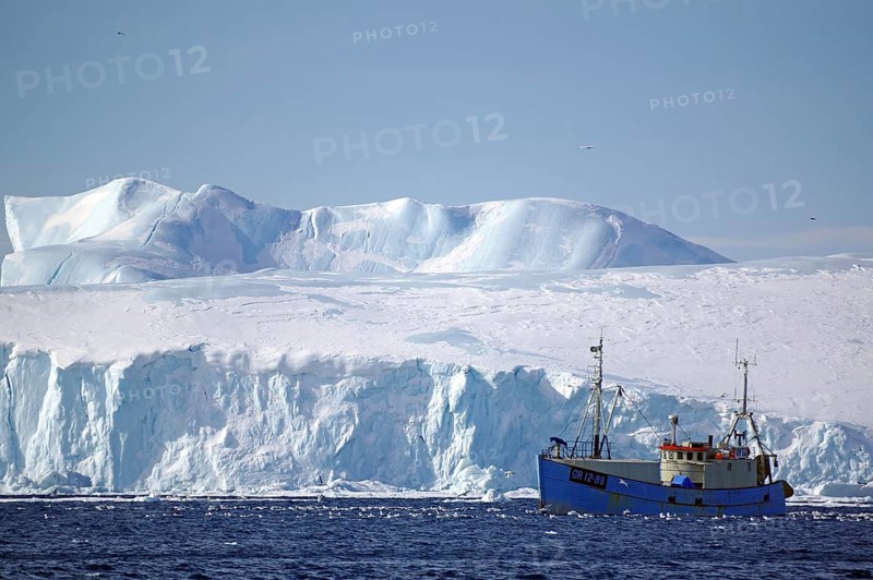 Small fishing boat in front of huge icebergs and drift ice