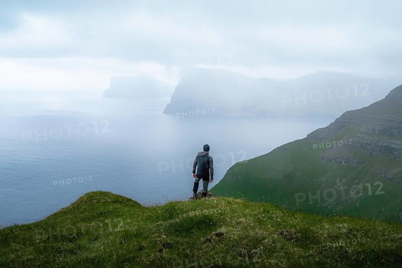Person standing on the mountain looking at the village of Mikladalur