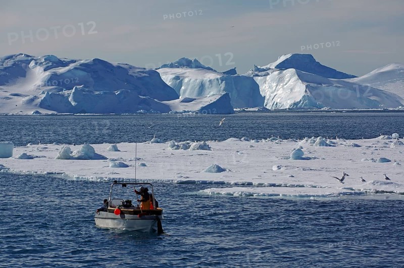 Small fishing boat in front of huge icebergs and drift ice