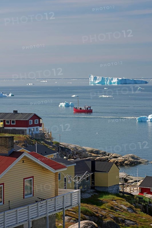 Wooden houses in front of a bay with fishing boat and icebergs