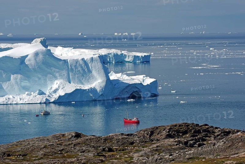 Red fishing boat in a bay with huge icebergs