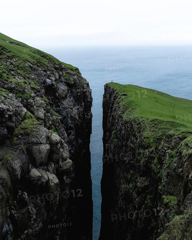 Small person standing on cliff with deep crevice