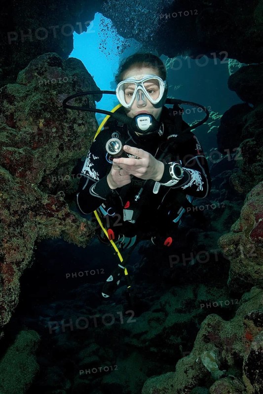 Young woman with scuba diving equipment dives into cave