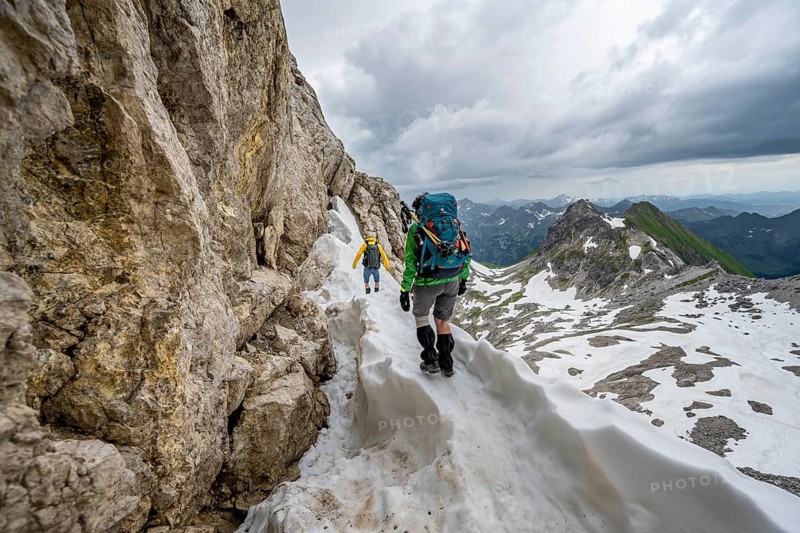 Hiker and hiker on snow remains in rocky terrain