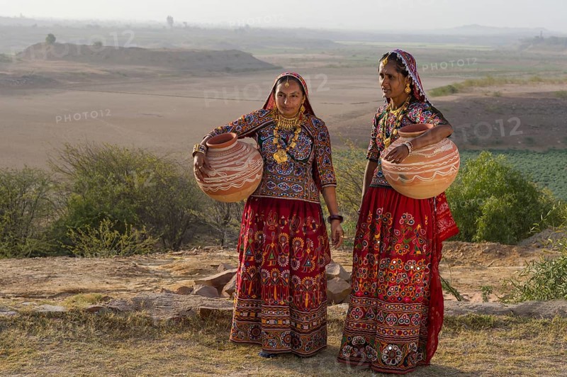 Two Ahir woman in traditional colorful dress carrying water in a clay jug