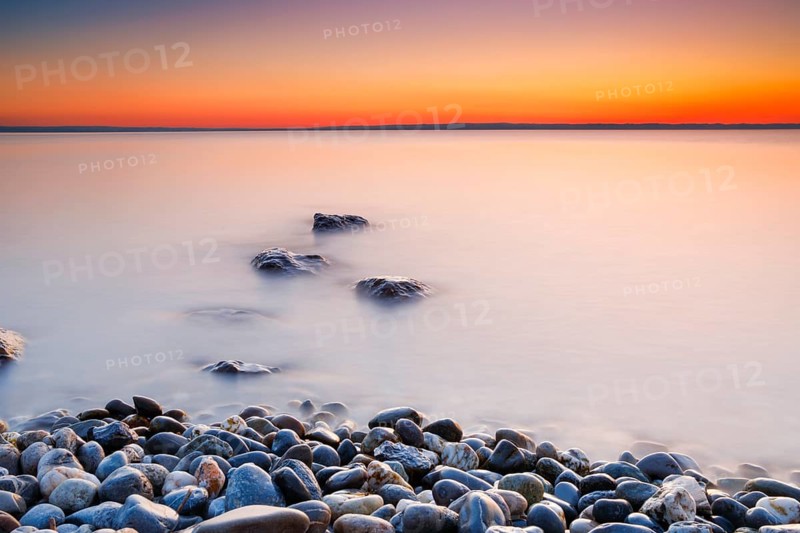 View over Lake Constance at sunrise with stones in the foreground and photographed with slow shutter speed