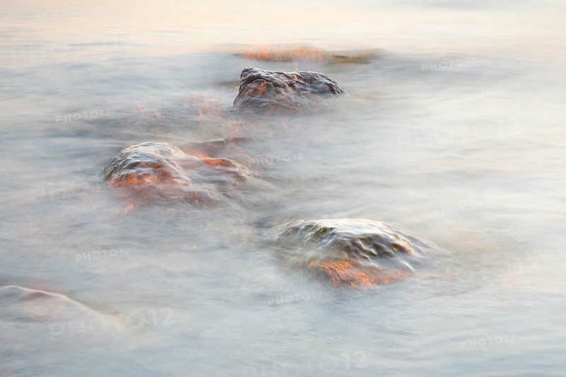 Light play and stones in the water at sunrise photographed with slow shutter speed
