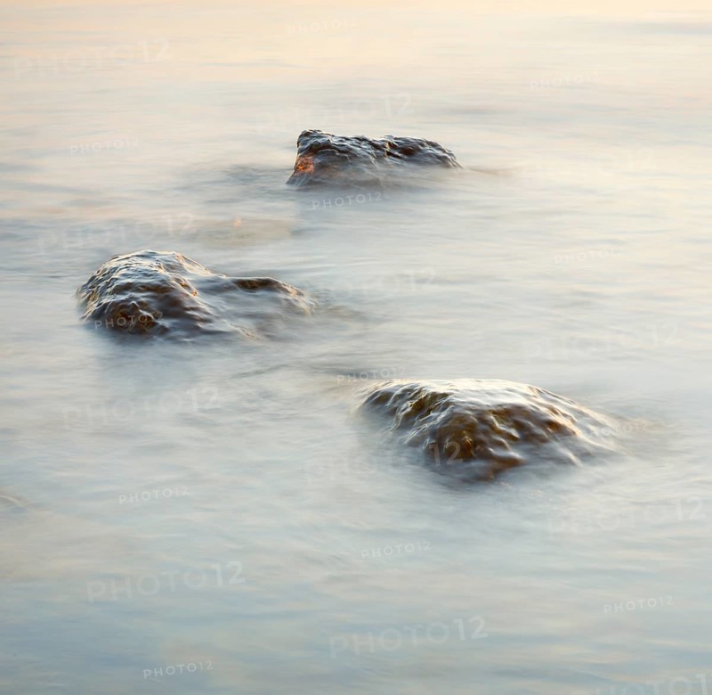 Light play and stones in the water at sunrise photographed with slow shutter speed