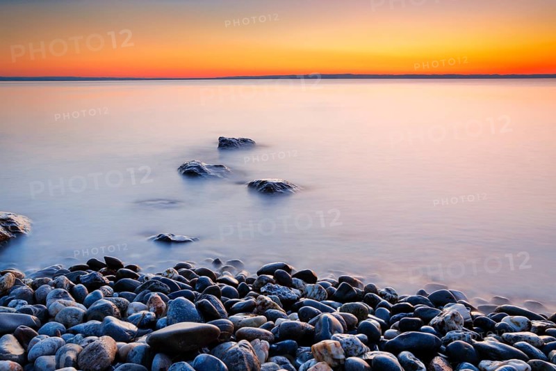 View over Lake Constance at sunrise with stones in the foreground and photographed with slow shutter speed