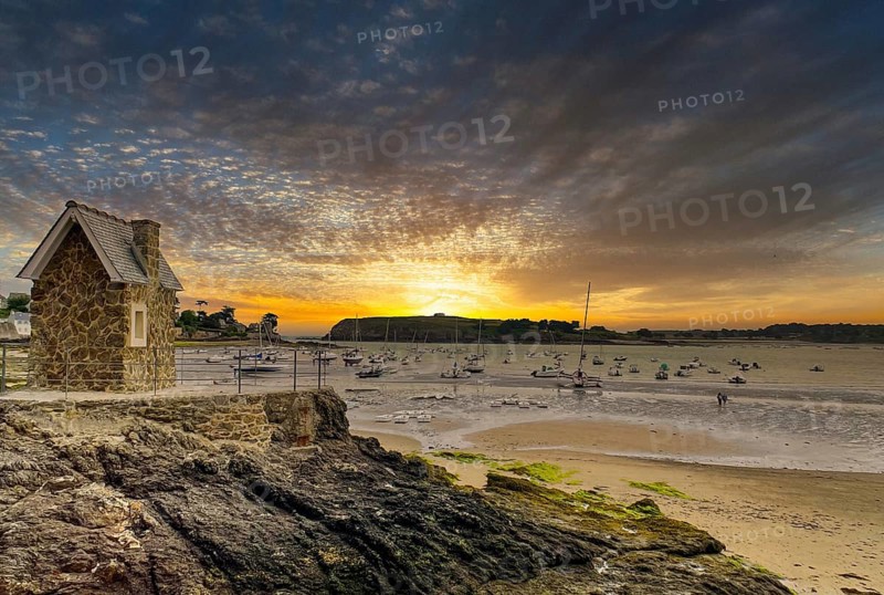 Small harbour at low tide with fishing boats and a small stone house at a dramatic sunrise
