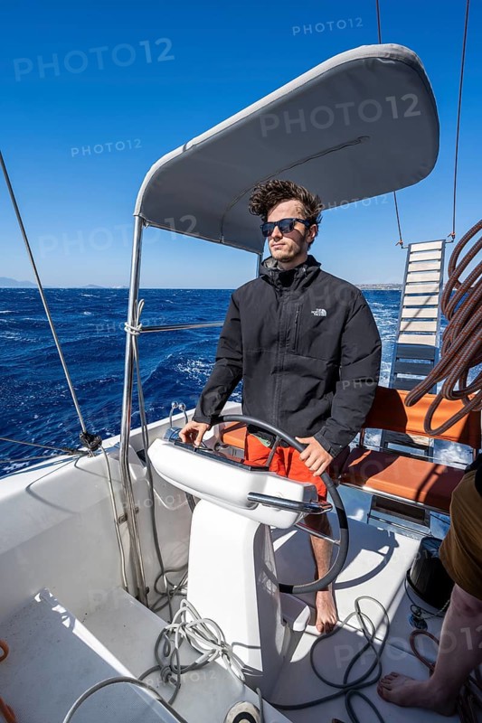 Man at the wheel in the cockpit on the deck of a sailing catamaran