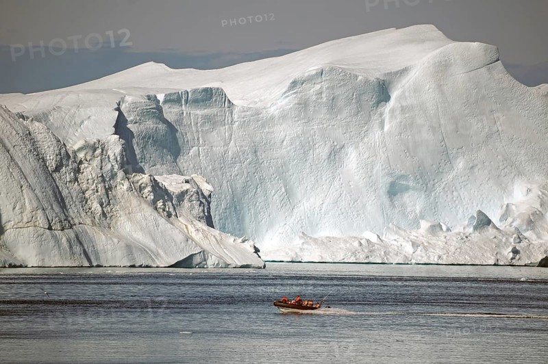 Boat with passengers in front of huge iceberg