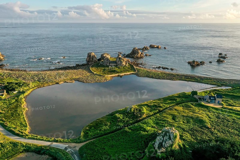 Drone shot from the mainland of the granite coast and the house between the rocks (Le gouffre de Plougrescant) in the morning and the Atlantic Ocean