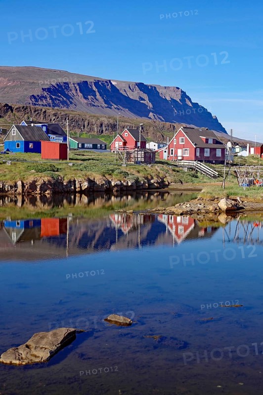 Wooden houses reflected in the water in front of mountains