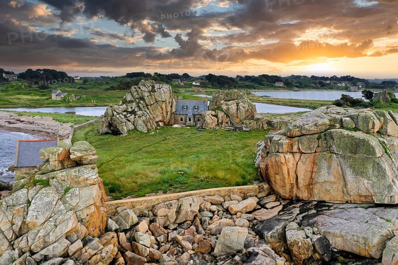 Drone shot from the Atlantic Ocean onto the granite coast of Plougrescant with a view of the house between the rocks (Le gouffre de Plougrescant) at sunset