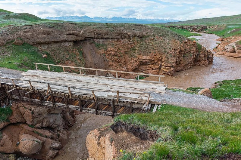 Wooden bridge over a muddy river flowing in a wild gorge