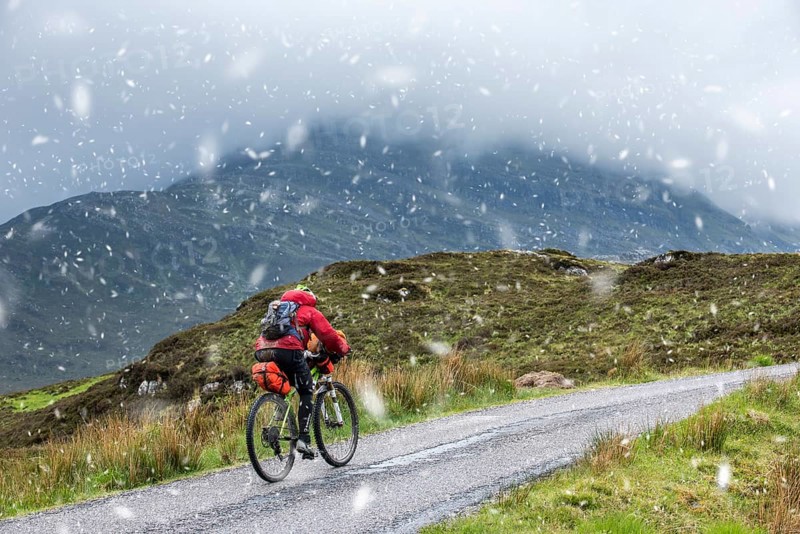 Lone cyclist on heavily laden touring bike on single track road through the Scottish Highlands in spring sleet