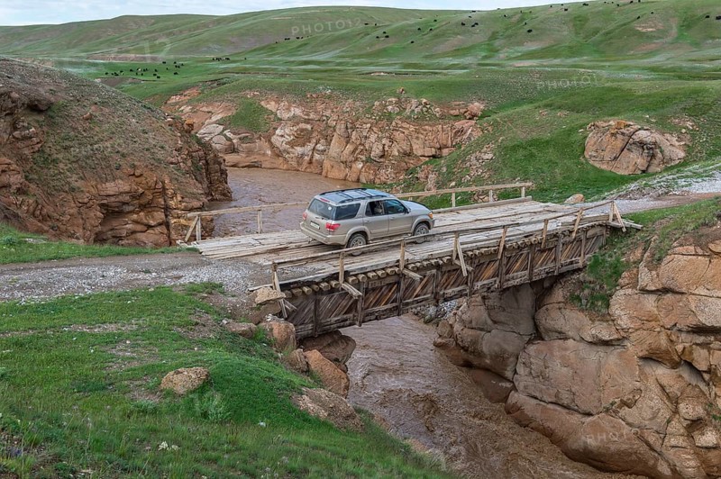 Off-road vehicle crossing a wooden bridge over a wild gorge