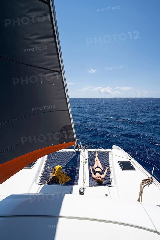 Young woman lying in the net on the deck of a sailing catamaran