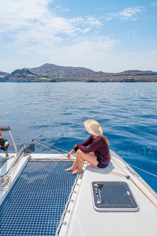 Young woman with hat sitting on deck at the net of a sailing catamaran