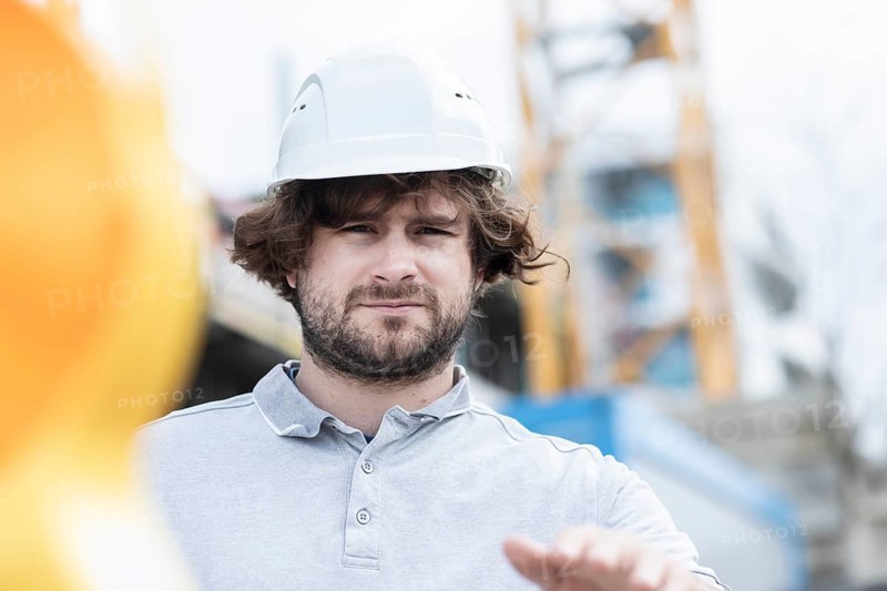 Technician with beard middle aged and wearing polo shirt and helmet outside at work