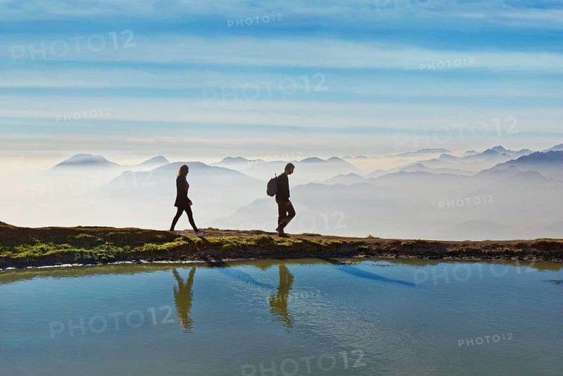 Hikers on a small lake with the peaks of the Lake Garda mountains and Bergamo Alps
