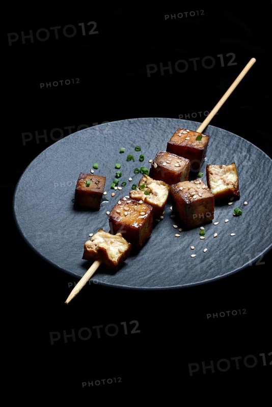 Fried tofu cubes with wooden skewer on plate