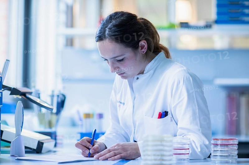 Lab technician with sample in petri dish works in a lab with lab equipment and writes protocol