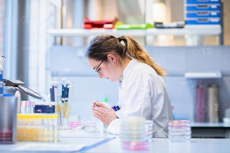 Lab technician with sample in petri dish working in a lab with lab equipment