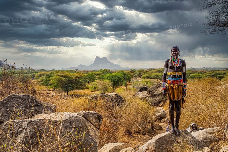Traditional dressed young girl from the Laarim tribe standing on a rock