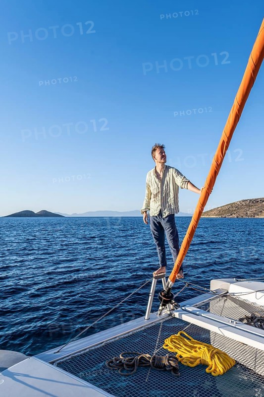 Young man standing by the furled headsail