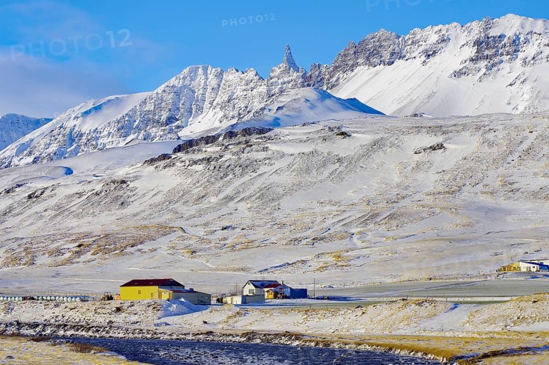 River and farm in front of snow-capped mountains