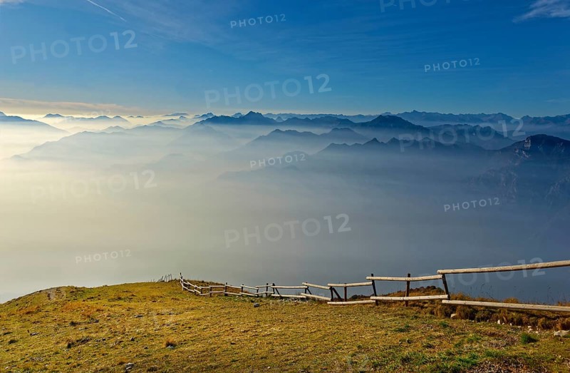 Meadow with fence and Lake Garda in the morning mist with Lake Garda mountains and Bergamo Alps
