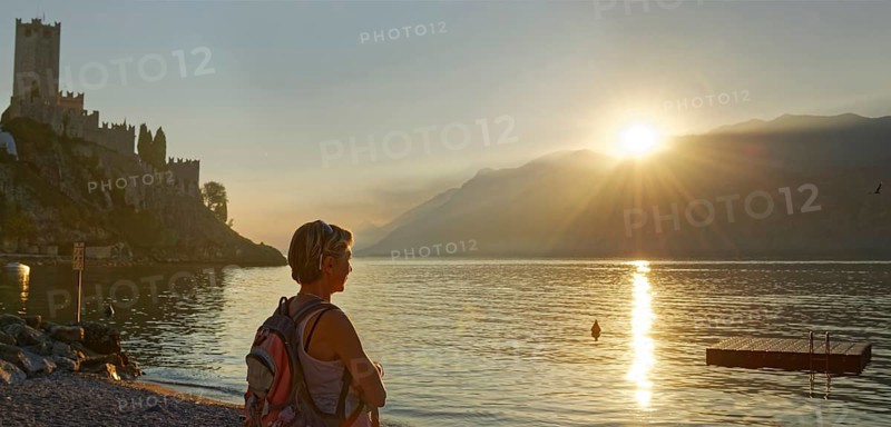 Hiker on the shore in front of Castello Scaligero at sunset