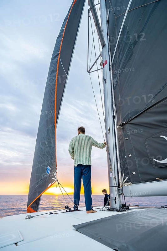 Young man standing leaning against the mast on a catamaran