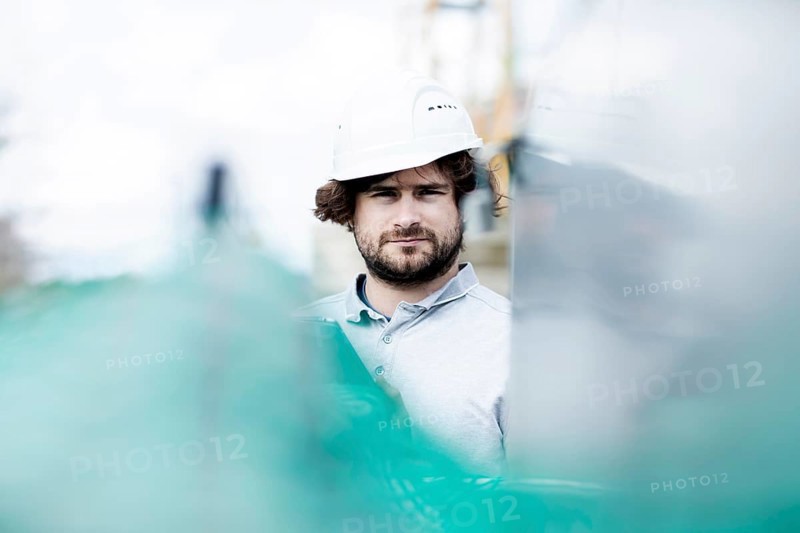 Technician with beard middle aged and wearing polo shirt and helmet outside at work